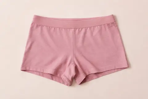 Shorty boxer rose sans couture posé à plat sur un fond crème, avec sa maille extensible et sa coupe couvrante.