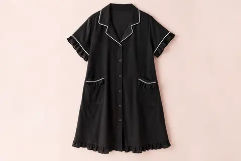 Chemise de nuit noire en coton, boutonnée sur le devant, avec poches et finitions blanches contrastantes.