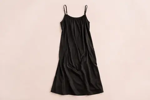 Fond de robe long noir à fines bretelles réglables, présenté à plat sur un fond crème.