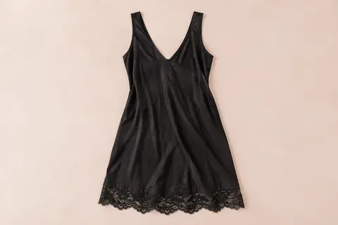 Nuisette noire sans manches en coton, avec col en V et ourlet en dentelle ajourée sur fond crème.