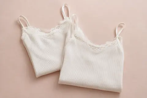 Deux caracos blancs en coton côtelé à fines bretelles, avec des détails de dentelle sur fond crème.