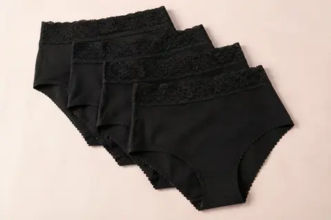 Lot de cinq culottes taille haute noires en coton avec une large ceinture en dentelle, sur fond crème.